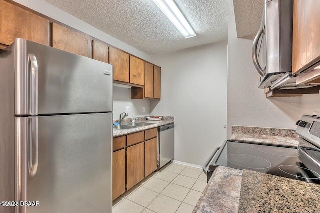 kitchen featuring brown cabinetry, appliances with stainless steel finishes, light tile patterned flooring, a textured ceiling, and a sink