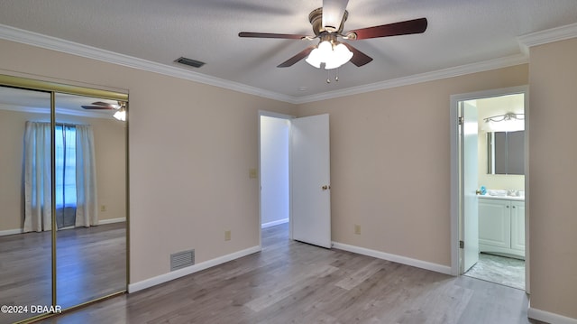 unfurnished bedroom featuring light wood-type flooring, ensuite bath, ceiling fan, crown molding, and a closet