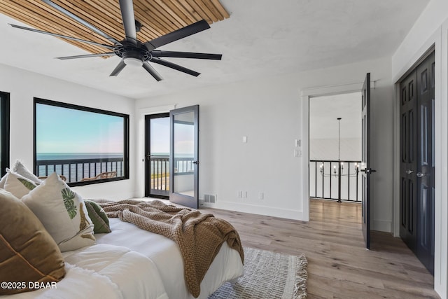 bedroom with a water view, access to exterior, ceiling fan with notable chandelier, and light hardwood / wood-style flooring