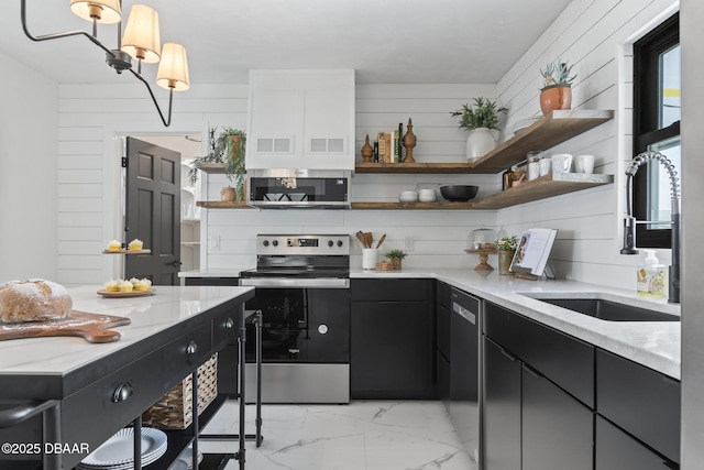 kitchen with appliances with stainless steel finishes, wooden walls, sink, hanging light fixtures, and light stone countertops