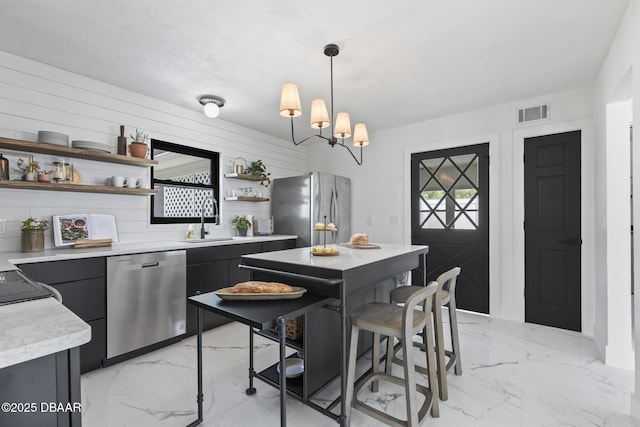 kitchen featuring pendant lighting, wood walls, sink, a chandelier, and stainless steel appliances