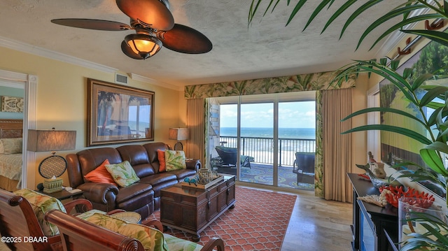 living area with a textured ceiling, a water view, wood finished floors, visible vents, and ornamental molding