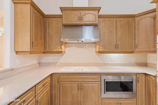 kitchen with light stone counters, wall chimney range hood, white electric stovetop, decorative backsplash, and stainless steel microwave