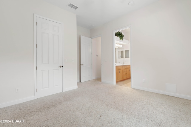 unfurnished bedroom featuring light carpet and ensuite bath