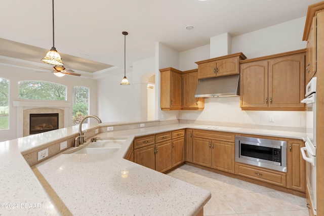 kitchen with stainless steel microwave, sink, light stone countertops, stovetop, and decorative light fixtures