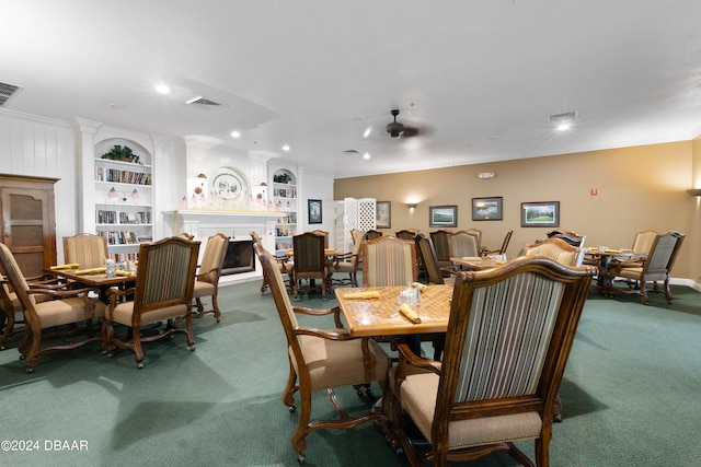 carpeted dining space with a large fireplace, built in features, ceiling fan, and crown molding