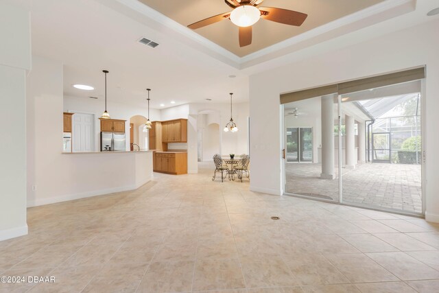 unfurnished living room with a tray ceiling, light tile patterned floors, and ceiling fan with notable chandelier