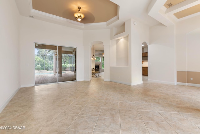 tiled empty room with ceiling fan, a high ceiling, and a tray ceiling