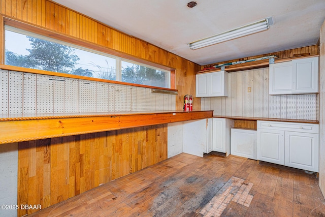 kitchen with wood-type flooring, wooden walls, white cabinets, and a wealth of natural light