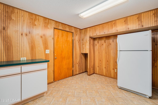 kitchen with freestanding refrigerator, wood walls, a textured ceiling, and dark countertops