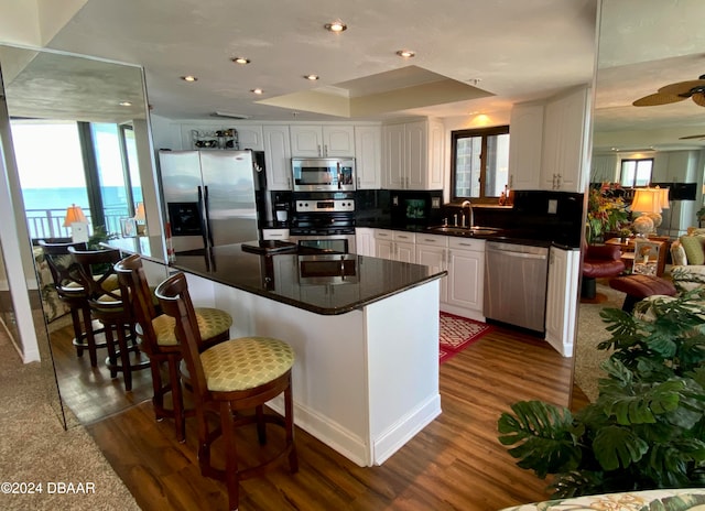 kitchen with stainless steel appliances, white cabinetry, dark hardwood / wood-style floors, a breakfast bar area, and a water view