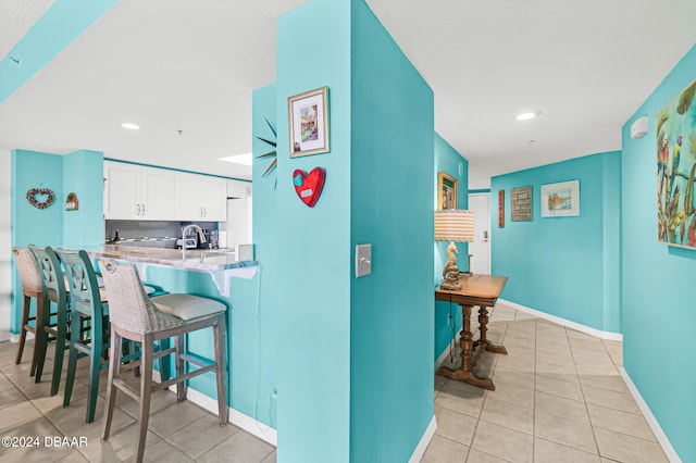 kitchen featuring a kitchen bar, light tile patterned floors, sink, white cabinets, and kitchen peninsula