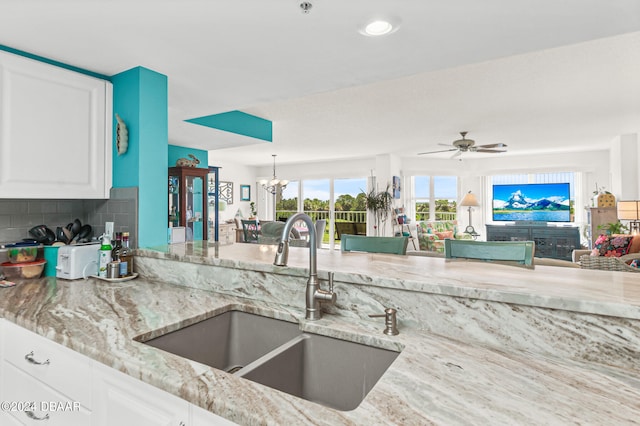 kitchen with white cabinets, ceiling fan with notable chandelier, sink, and backsplash