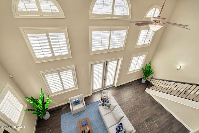 living room with dark wood-type flooring, ceiling fan, and a towering ceiling