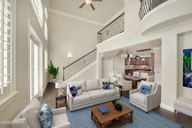 living room with hardwood / wood-style floors, a high ceiling, ceiling fan with notable chandelier, and crown molding