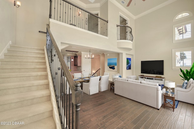 living room featuring a towering ceiling, ceiling fan with notable chandelier, dark wood-type flooring, and crown molding