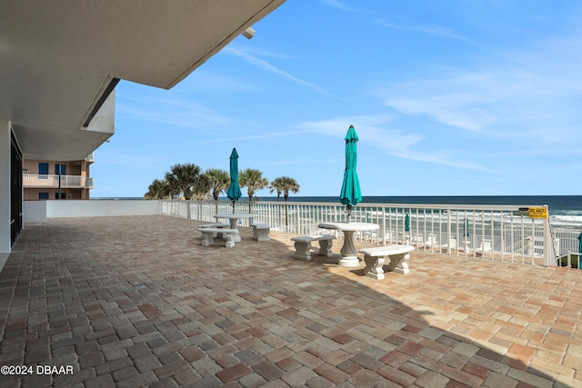 view of patio with a balcony, a beach view, and a water view