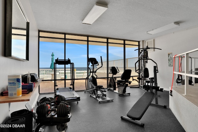 gym with expansive windows, a water view, and a textured ceiling