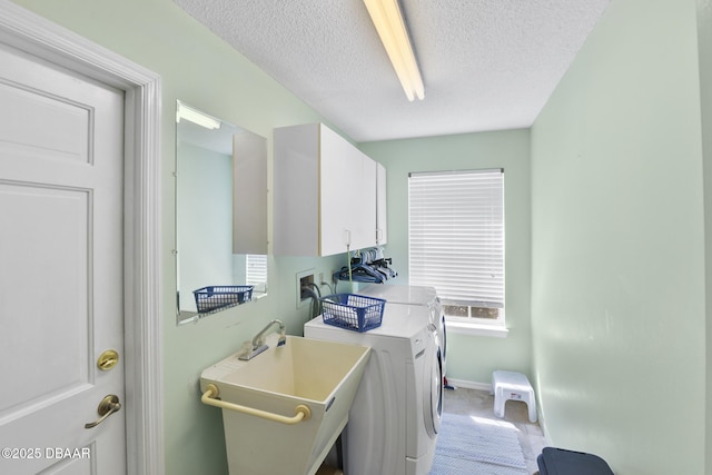 clothes washing area with washer and dryer, a sink, a textured ceiling, cabinet space, and baseboards