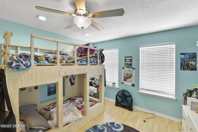 bedroom featuring ceiling fan, baseboards, a textured ceiling, and wood finished floors