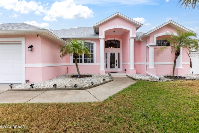 entrance to property with french doors, a garage, and a lawn