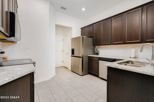 kitchen featuring dark brown cabinetry, light stone countertops, a sink, stainless steel appliances, and tasteful backsplash