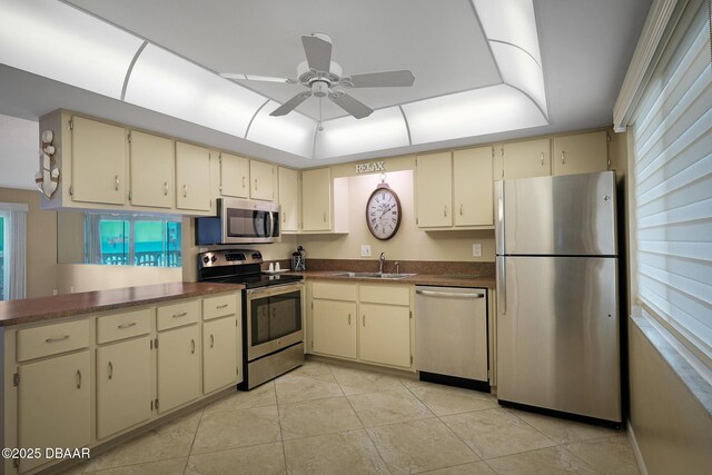 kitchen featuring a tray ceiling, stainless steel appliances, cream cabinets, and sink