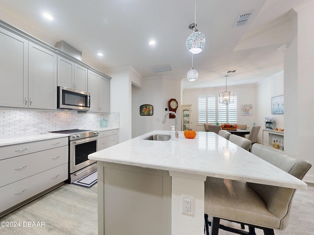 kitchen featuring sink, a breakfast bar, gray cabinetry, stainless steel appliances, and an island with sink