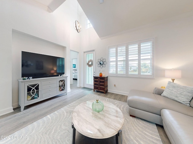 living room featuring ornamental molding, a towering ceiling, wood-type flooring, and a notable chandelier