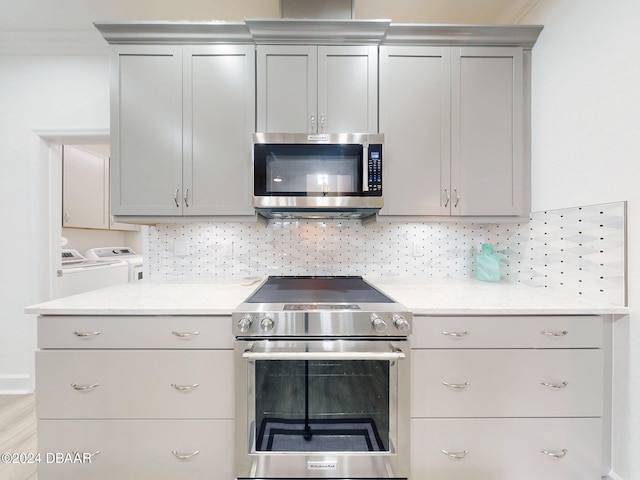 kitchen with gray cabinetry, washer and dryer, stainless steel appliances, light hardwood / wood-style floors, and backsplash