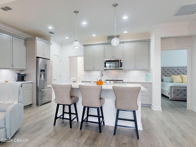 kitchen featuring decorative light fixtures, light wood-type flooring, appliances with stainless steel finishes, gray cabinets, and an island with sink