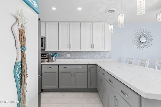 kitchen with gray cabinetry, backsplash, a kitchen bar, hanging light fixtures, and kitchen peninsula