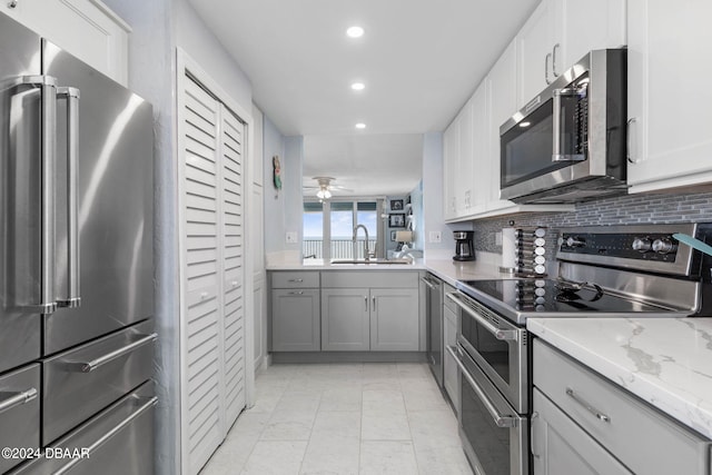 kitchen featuring sink, tasteful backsplash, ceiling fan, light stone countertops, and appliances with stainless steel finishes