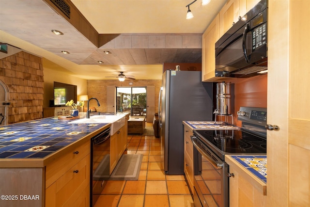 kitchen featuring open floor plan, tile countertops, light tile patterned flooring, black appliances, and a sink