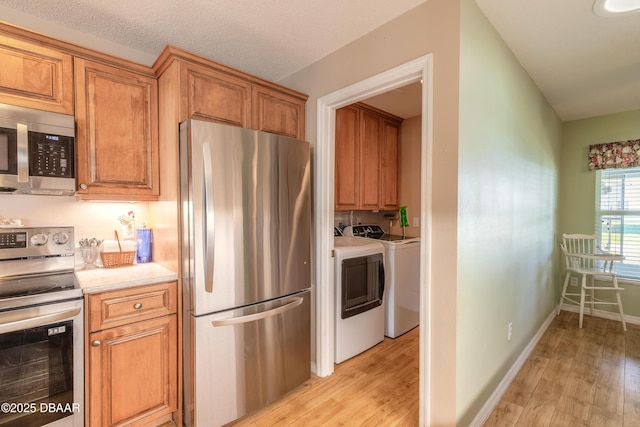 kitchen with appliances with stainless steel finishes, light wood-type flooring, and washer and clothes dryer