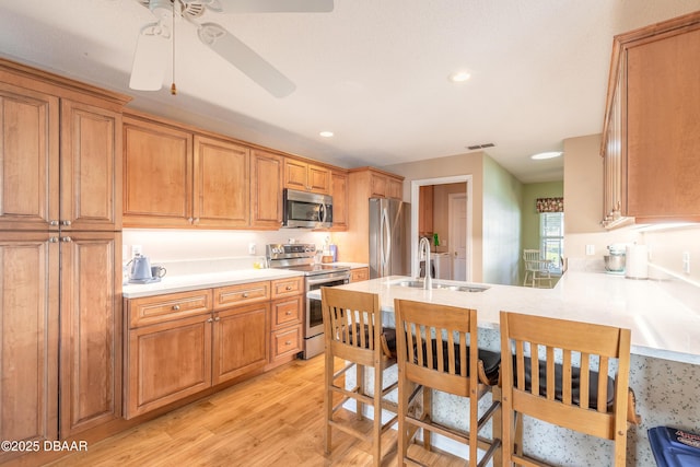 kitchen featuring ceiling fan, sink, stainless steel appliances, light hardwood / wood-style flooring, and kitchen peninsula