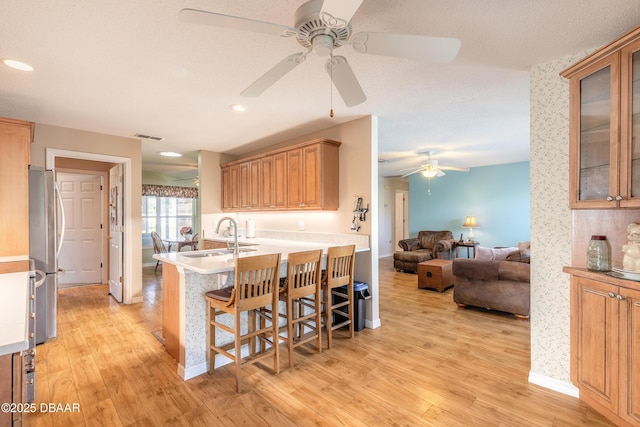 kitchen with kitchen peninsula, stainless steel fridge, light wood-type flooring, sink, and a breakfast bar area