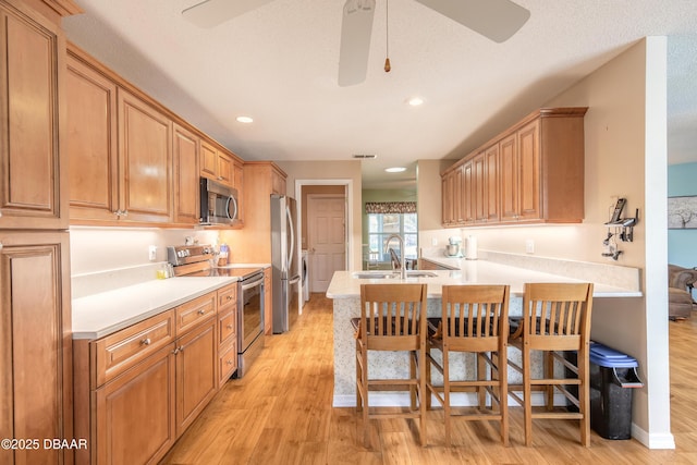 kitchen with sink, ceiling fan, a kitchen bar, kitchen peninsula, and stainless steel appliances