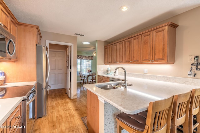 kitchen featuring kitchen peninsula, stainless steel appliances, sink, light hardwood / wood-style flooring, and a breakfast bar area