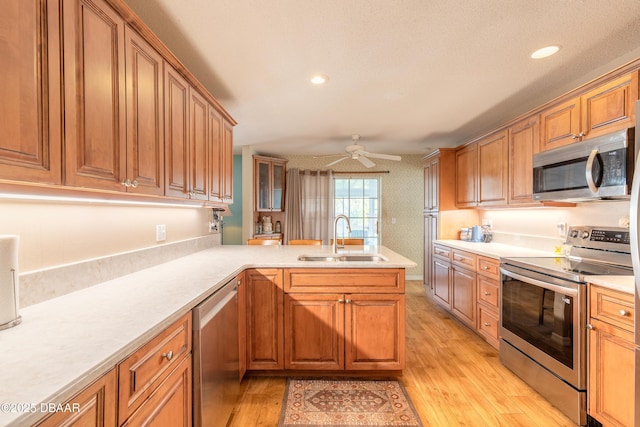 kitchen featuring ceiling fan, sink, light hardwood / wood-style flooring, kitchen peninsula, and appliances with stainless steel finishes