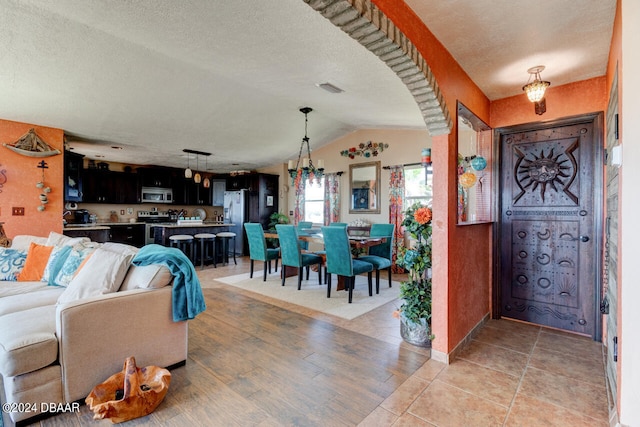 living room featuring a textured ceiling, an inviting chandelier, and vaulted ceiling