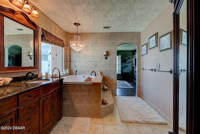 bathroom featuring vanity, a relaxing tiled tub, an inviting chandelier, tile walls, and tile patterned flooring