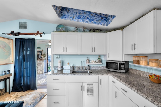 kitchen with light stone counters, ceiling fan, sink, white cabinets, and lofted ceiling