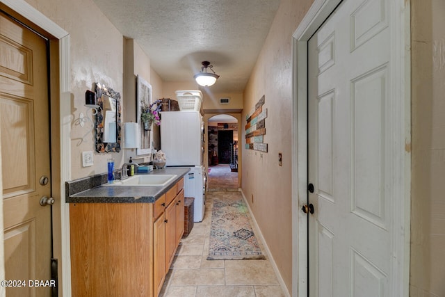 laundry area with sink, light tile patterned floors, a textured ceiling, and stacked washer and dryer