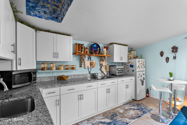 kitchen featuring sink, light tile patterned floors, light stone counters, white refrigerator, and white cabinets