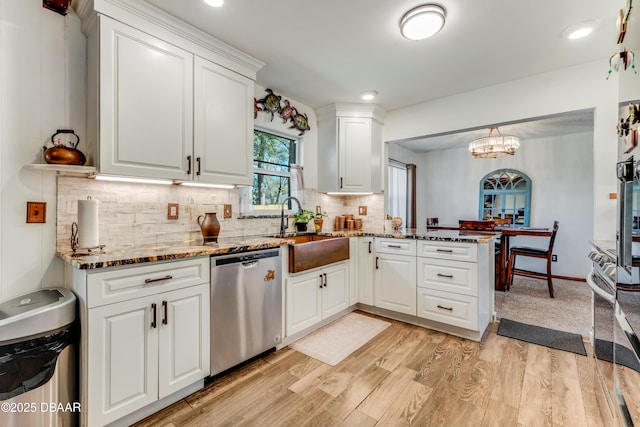 kitchen featuring pendant lighting, sink, white cabinetry, stainless steel dishwasher, and kitchen peninsula