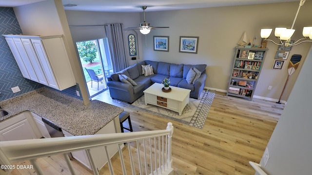 living room with ceiling fan with notable chandelier and light wood-type flooring