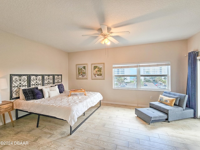 bedroom featuring light hardwood / wood-style floors, ceiling fan, and a textured ceiling