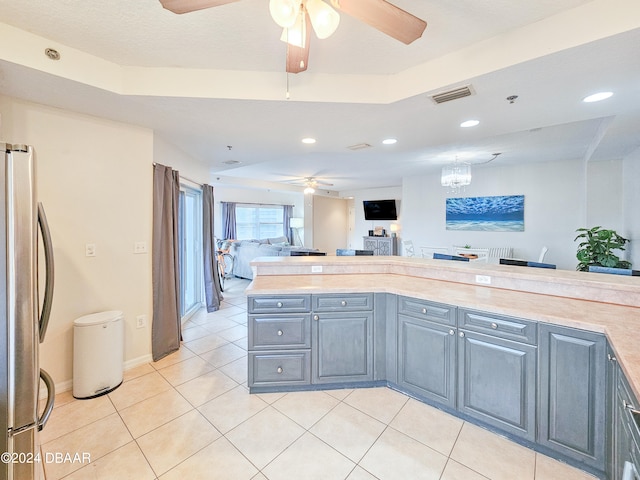 kitchen with ceiling fan with notable chandelier, light tile patterned floors, a raised ceiling, and stainless steel refrigerator