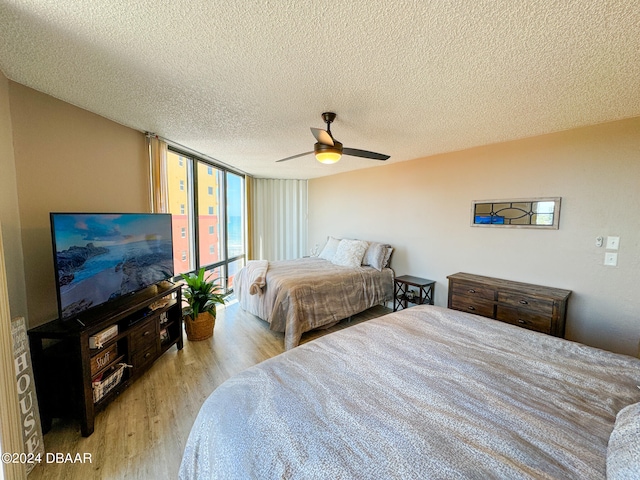 bedroom with expansive windows, light hardwood / wood-style floors, ceiling fan, and a textured ceiling